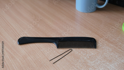 Tableau sur toile Black plastic comb and hairpin lying on light wooden table .