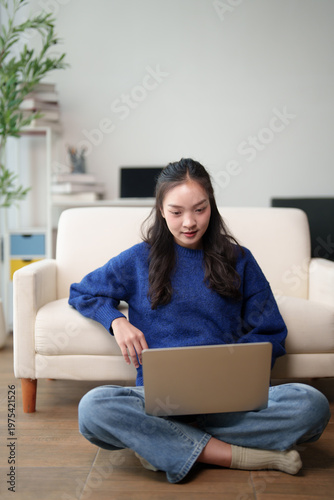 Asian young woman working or studying from home, remotely connecting on laptop, sitting cross-legged on floor enjoying modern lifestyle and comfortable living space