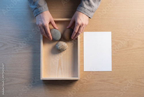 Woman's hands arranging stones in a wooden box with paper