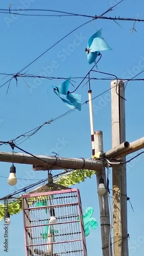 Blue plastic wind spinners attached to wires and bamboo structure under clear sky
