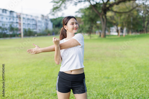 Young woman stretching arm, exercising outdoors in park