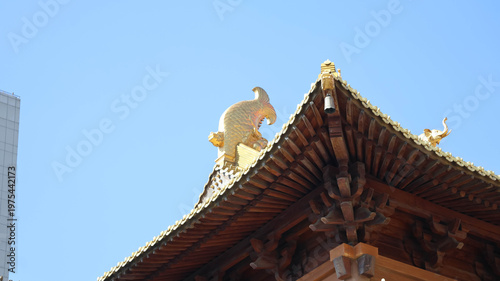 Tableau sur toile An Asian style structure adorned with intricate wooden patterns and vibrant gold accents, which is a pagoda like structure situated in what appears to be a cityscape under a clear blue sky