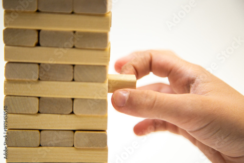 Close-up of a tower made of wooden bars, a game of gengo, stands on a white background, from the side a hand takes out a wooden block starting the game. The concept of board games, business