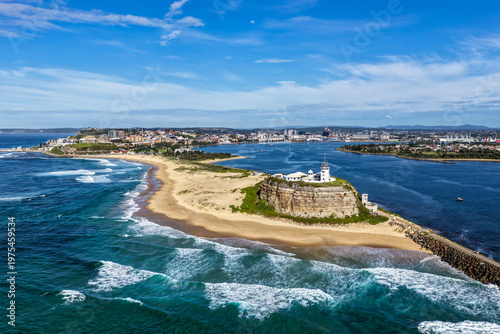 Aerial drone view of Nobbys Lighthouse and sandy Nobbys Beach with Newcastle city skyline and working harbour in the background.