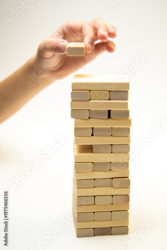 A tower made of wooden bars, a game of gengo, stands on a white background, from which the hand took out a wooden block and is going to put it on top starting the game. The concept of board games