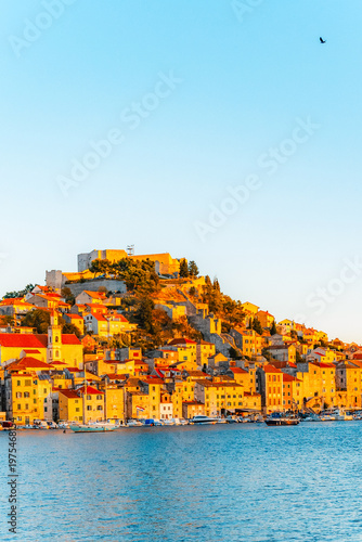 evening at Banj beach with a view of the historic Sibenik city center and fortress under a colorful sunset sky, Croatia.