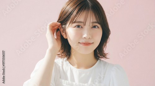 Close up portrait of a smiling Japanese woman touching her hair on a pink background