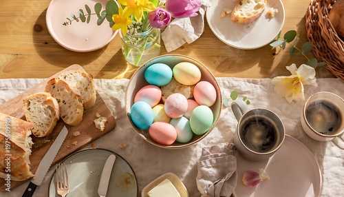 Overhead view of a festive Easter brunch table setting with colorful eggs, fresh bread, butter, flowers, and steaming coffee