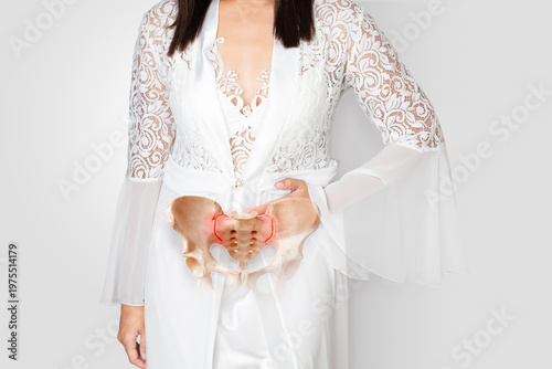 Pregnant woman in white satin nightwear holding lower abdomen due to pelvic pain, inflammation, or pregnancy discomfort isolated on white background