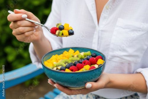 Fresh Fruit Salad Bowl with Mango, Kiwi, Blueberries and Raspberries Held by Woman Outdoors