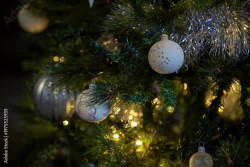 Un sapin de Noël illuminé, décoré pour les fêtes de fin d'année. Gros plan sur des décoration d'un sapin de noël artificiel, avec guirlande lumineuse en fond. 