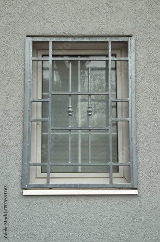 New white window with gray metal security decorative grille on stucco wall closeup