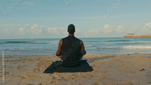 Back view of a man meditating in upward salute yoga pose on a tropical beach with calm waves and blue skies, capturing mindfulness, peace, and coastal serenity.