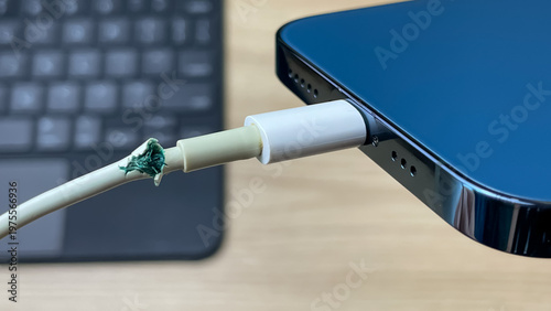 A close-up of a smartphone with a damaged charging cable attached. The worn insulation on the cable is visible. Conceptually, this illustrates the breakdown of electronics, wear.