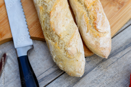 Fresh baked baguette bread loaves with knife on rustic wood