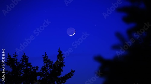 Blue hour time with crescent Moon, stars and planets above landscape silhouettes.