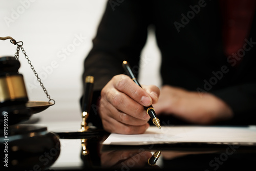 Close-up of a lawyer’s hand signing legal documents at a desk with judge gavel and scales of justice, law office background, selective focus.
