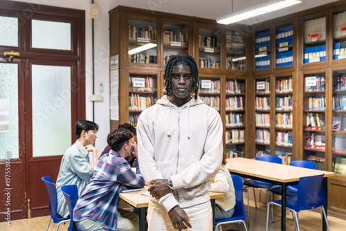 Black student standing in library with diverse classmates studying at tables. Capturing education, learning, and student life