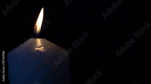 Single candle glows softly against black background. Candle flame flickers gently, casting gentle blue hue. Warm light contrasts stark darkness, evoking quiet reflection. Ideal for solemn moments
