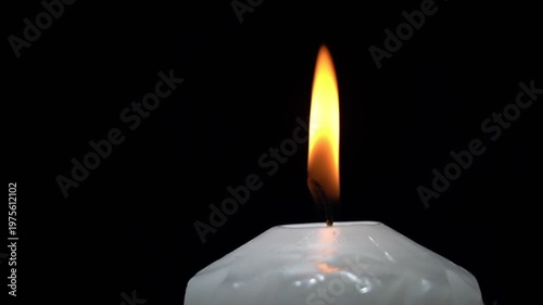 Single candle burns brightly against pure black background. Soft flame flickers, casting gentle glow. Candle wax shows subtle texture and warmth. Moment evokes calm, reflection, or quiet reverence