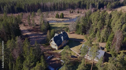 Aerial view of a large yellow house and smaller gray building surrounded by dense forest and open land, showcasing the natural landscape and rural setting
