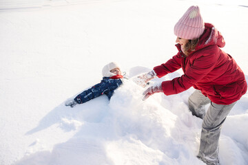 Mother and son playing together in the snow on a sunny winter day