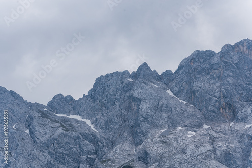 Massive grey rock face of Waxenstein mountains with dark green forest in summer
