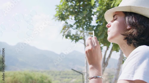 Cinematic side portrait of a young woman blowing soap bubbles. Mountain nature background, sunlight, camera movement, emotional softness, harmony and peaceful lifestyle feeling.