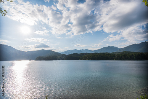 Sunny beach at Eibsee lake with turquoise water and green forest under bright sun at Zugspitze Mountain
