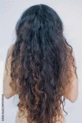Back view of young woman with long curly hair looking in the mirror