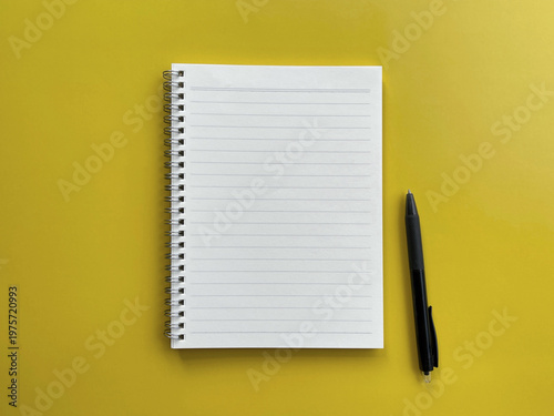 Minimalist workspace with blank lined notebook and pen on yellow background, top view copy space for ideas and planning