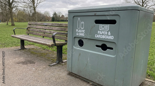 Recycling bin for plastic and cardboard near park bench  