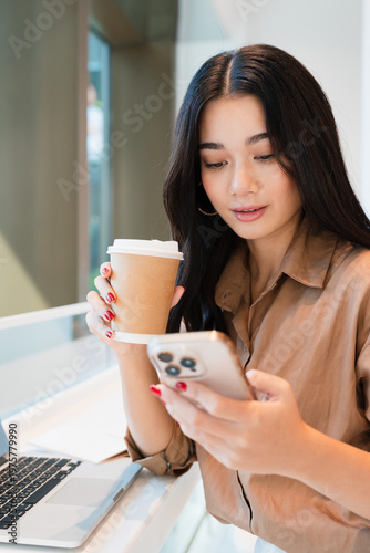 Young, confident, beautiful, professional Asian woman working at modern cafe, using, looking at smartphone.