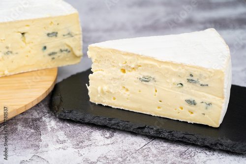 Tableau sur toile Wedge of creamy blue-veined brie on a black slate board