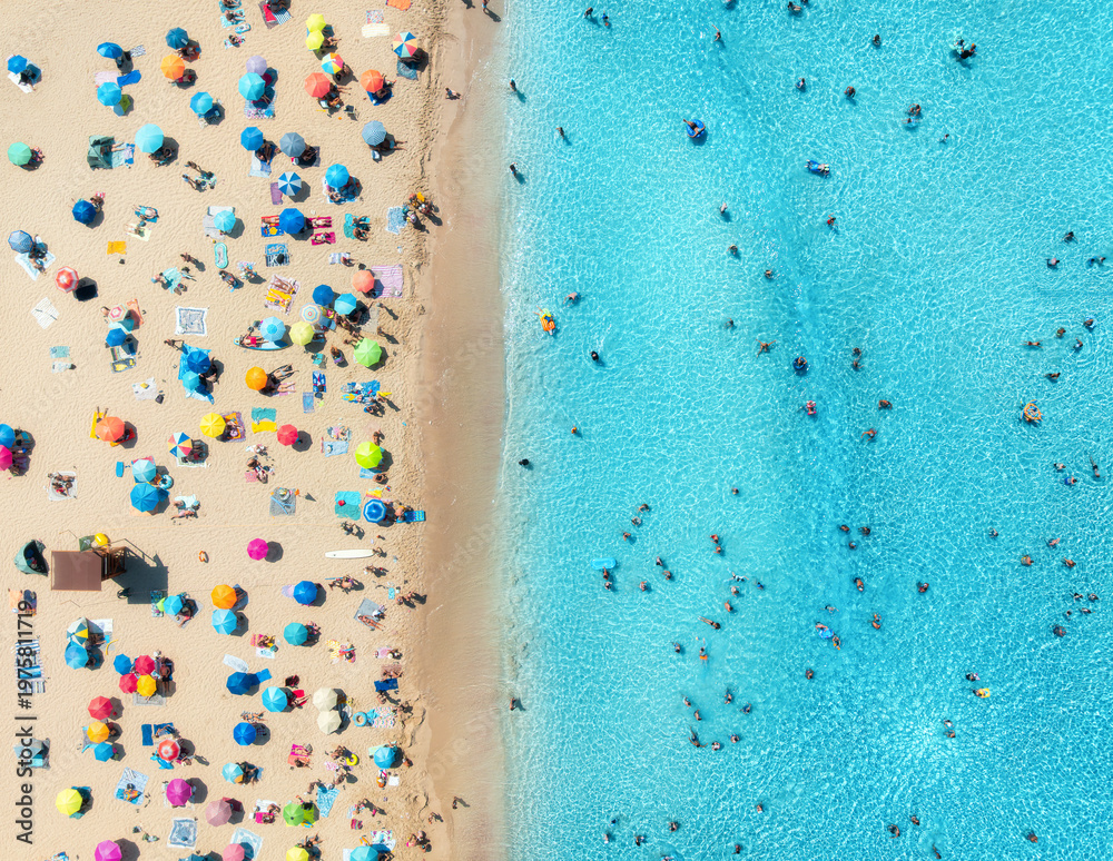 Fototapeta premium Aerial drone view of colorful umbrellas on sandy beach, swimming people in blue sea on sunny summer day. Top down view. Mallorca, Balearic Islands, Spain. Tropical. Clear turquoise water. Travel