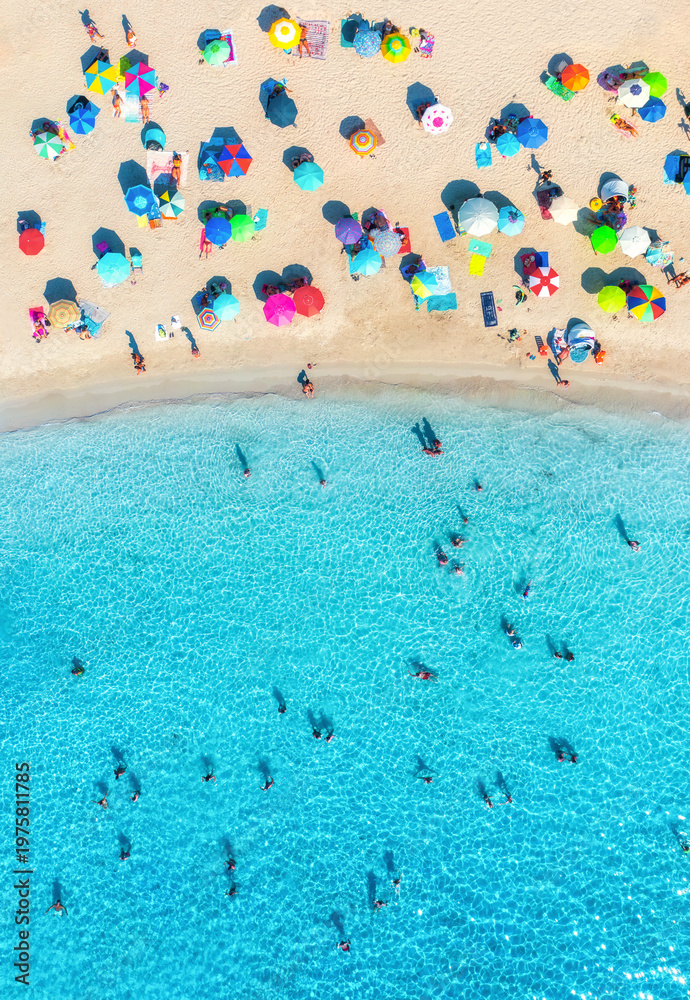 Fototapeta premium Aerial drone view of colorful umbrellas on sandy beach, swimming people in blue sea on sunny summer day. Top down view. Mallorca, Balearic Islands, Spain. Tropical. Clear turquoise water. Travel