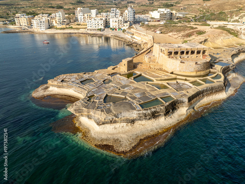 Aerial view of the ancient Qolla l-Bajda Salt Pans shimmer with geometric precision against the azure sea, Iz-Zebbug, Gozo, Malta.