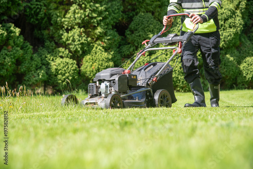 A person operates a lawn mower on a sunny day, worker cutting grass with lawn mower. Detailed view of gardening equipment in use, perfect for landscaping, maintenance, and outdoor service concepts