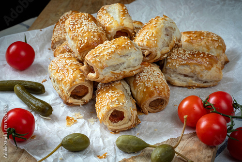 Hot Dog style sausages baked in puff pastry, sprinkled with sesame seeds, with capers, pickles and cherry tomatoes.