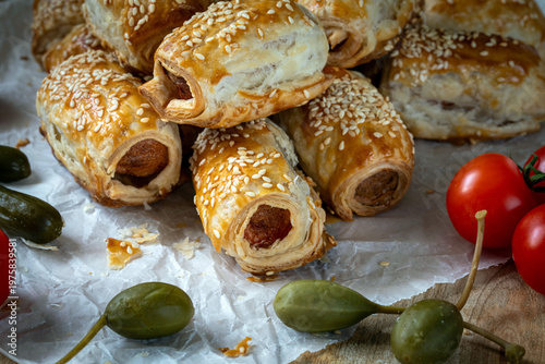 Hot Dog style sausages baked in puff pastry, sprinkled with sesame seeds, with capers, pickles and cherry tomatoes.
