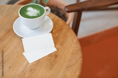 Two blank business card mockups and a cup of matcha latte on a round wooden table.