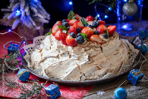 Meringue Pavlova cake with whipped cream frosting, decorated with berries and strawberries, against a festive backdrop on New Year's Eve.