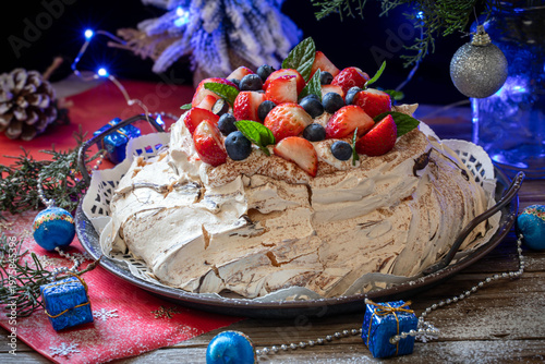 Meringue Pavlova cake with whipped cream frosting, decorated with berries and strawberries, against a festive backdrop on New Year's Eve.