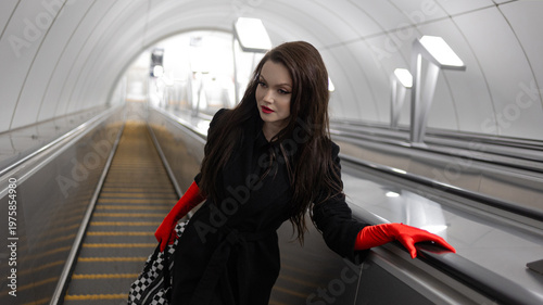 Stylish brunette climbing an escalator from a light-toned modern subway station