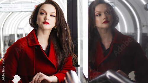 A dark-haired woman in a crimson coat on a metro platform, rushing for business
