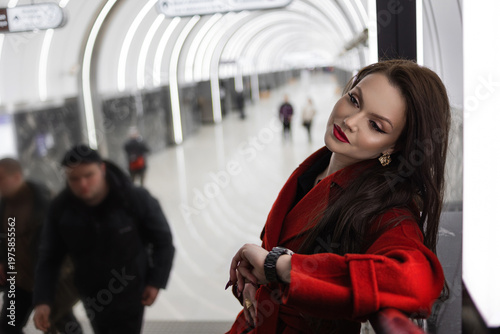 A stylish brunette in a red coat waiting for a train in the subway