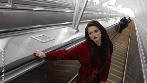 A young dark-haired woman in stylish clothes going up on an escalator from the subway