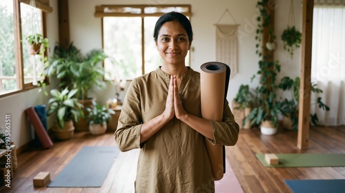Indian woman yoga instructor standing in studio holding mat with hands in prayer position. Small business owner and health wellness lifestyle banner with copy space