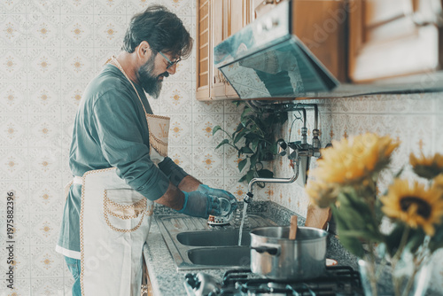 Tableau sur toile Bearded man washing dishes in a vintage kitchen wearing apron and gloves while d