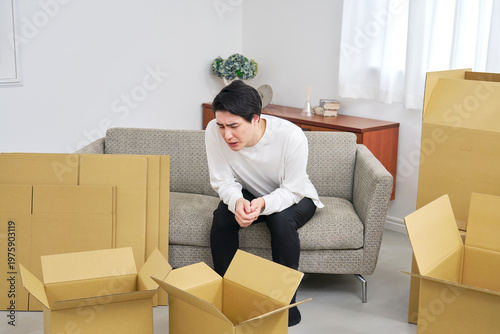 引っ越しの段ボールに囲まれ悩む若い男性